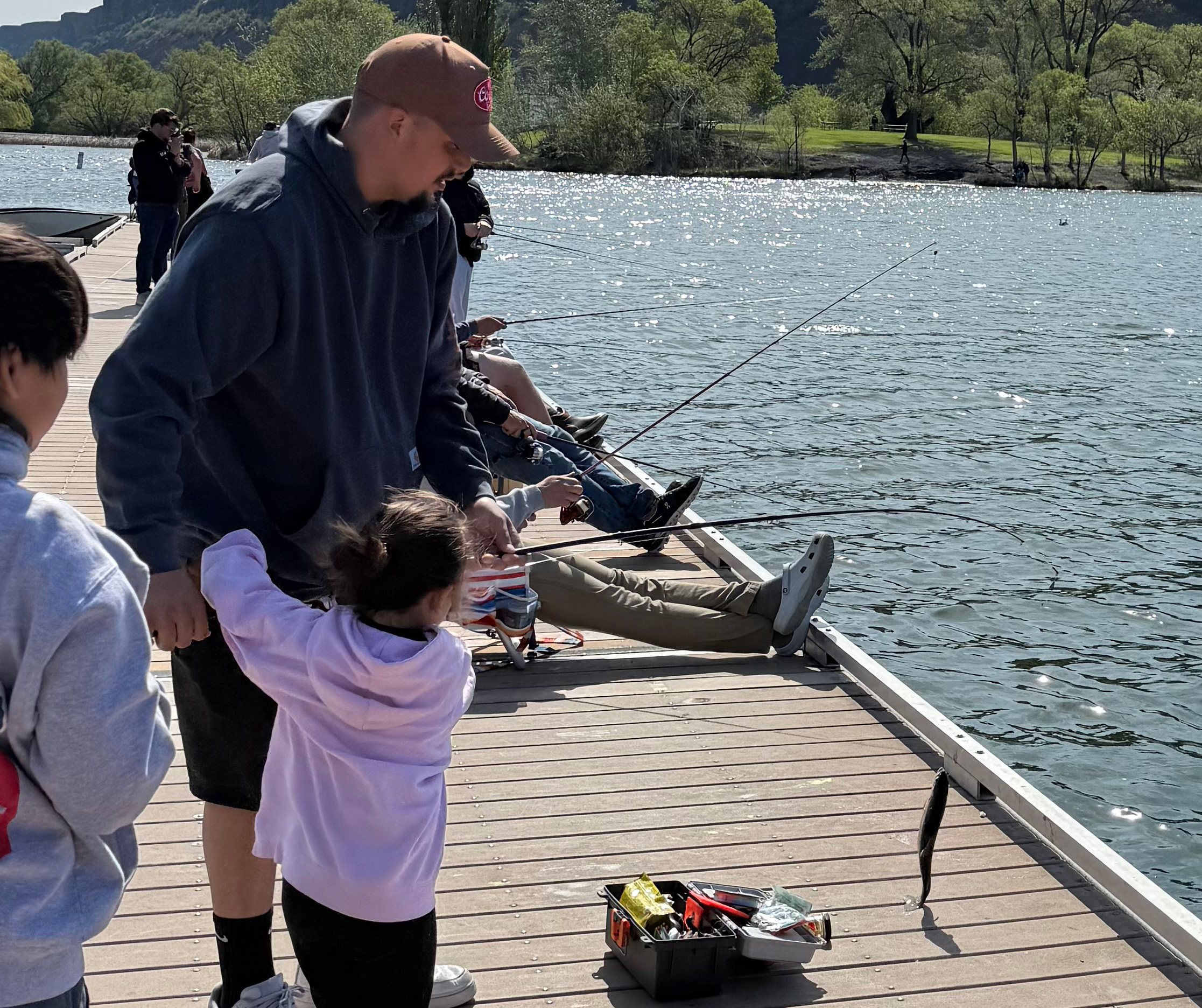 A dad helping his daughter land a trout from the dock at Park Lake during opening day.